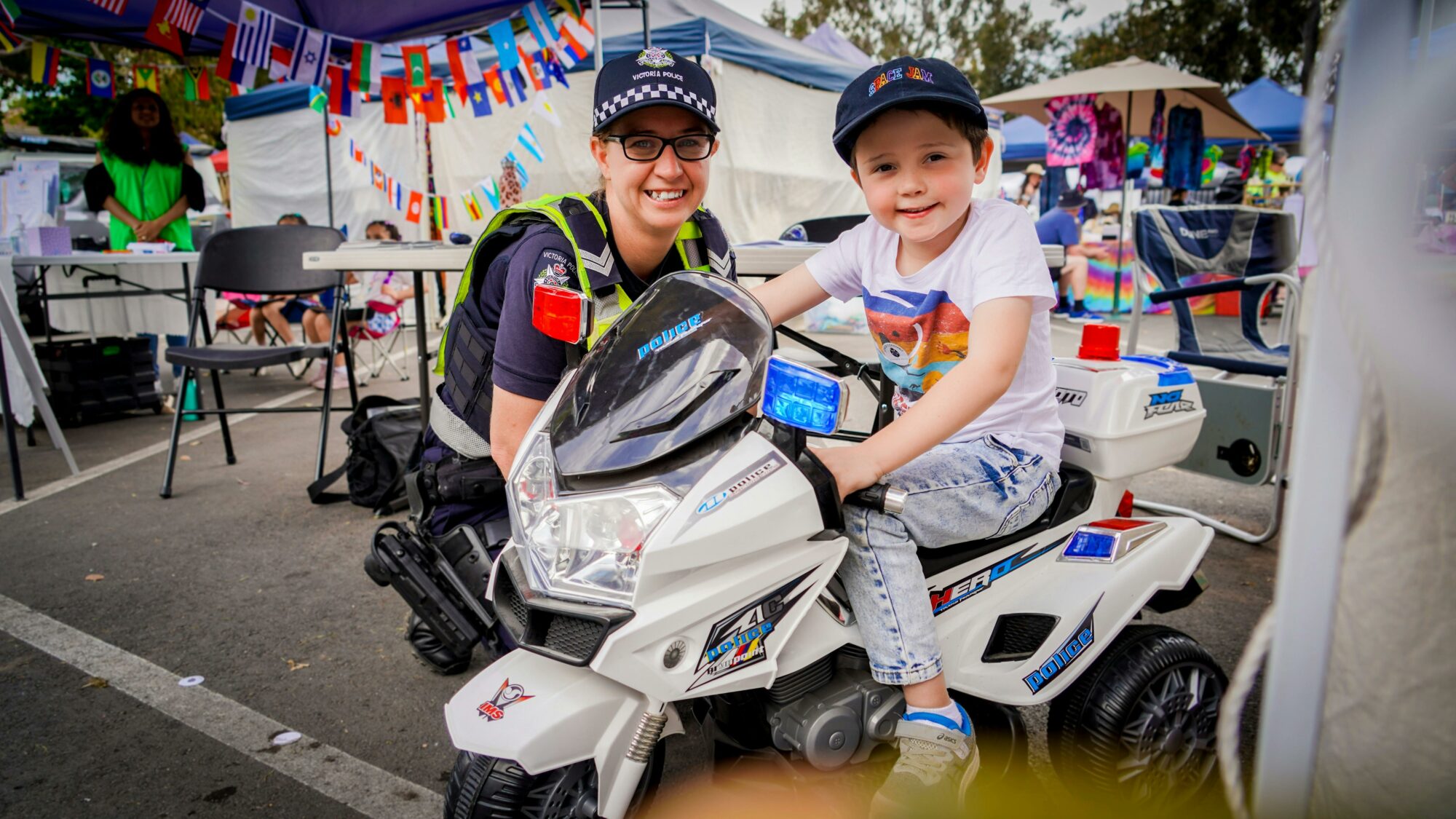 Young boy sitting on a police motor bike with female officer beside him.