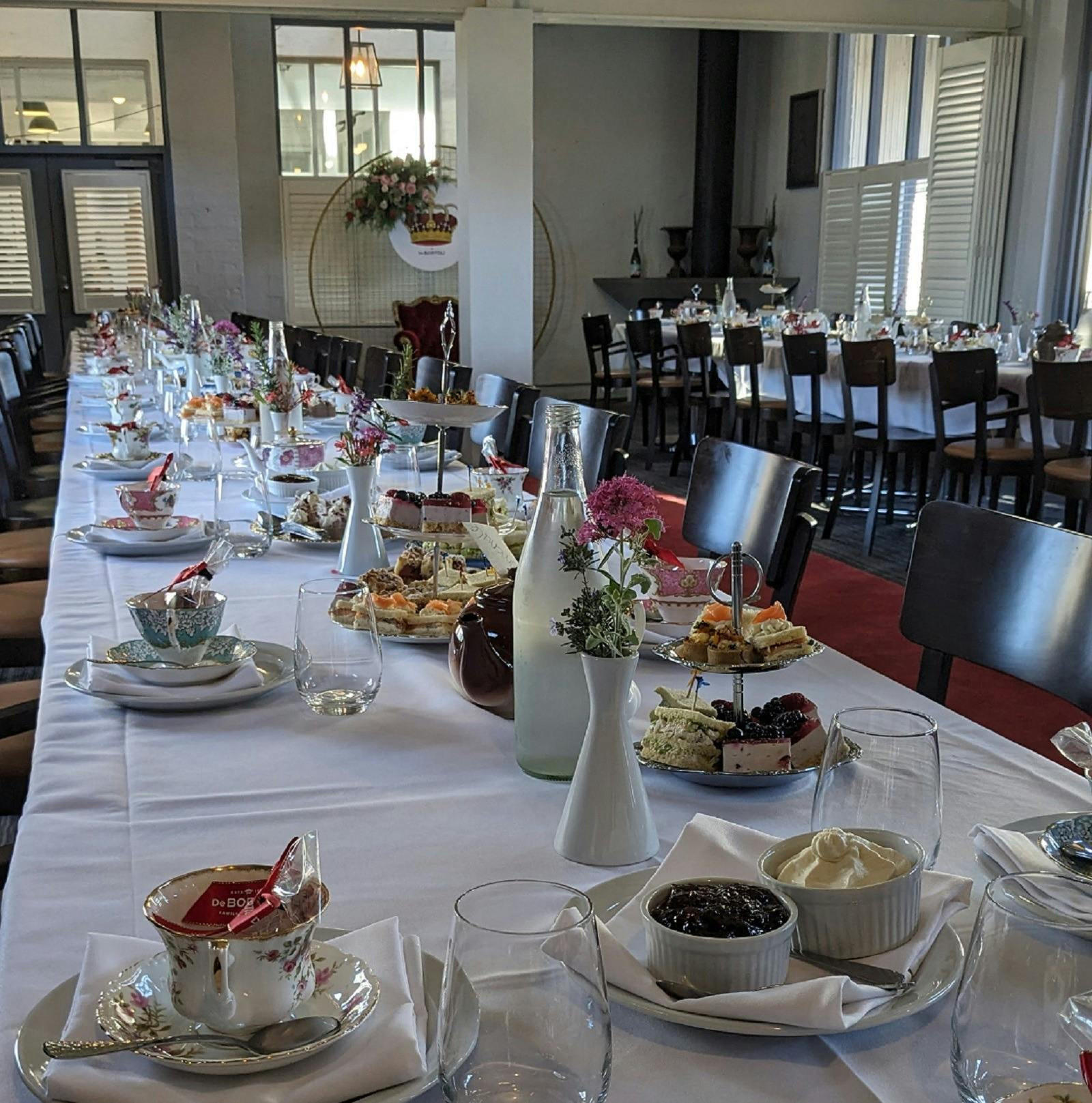 long table with dainty tea cups set out with food on tiered plates