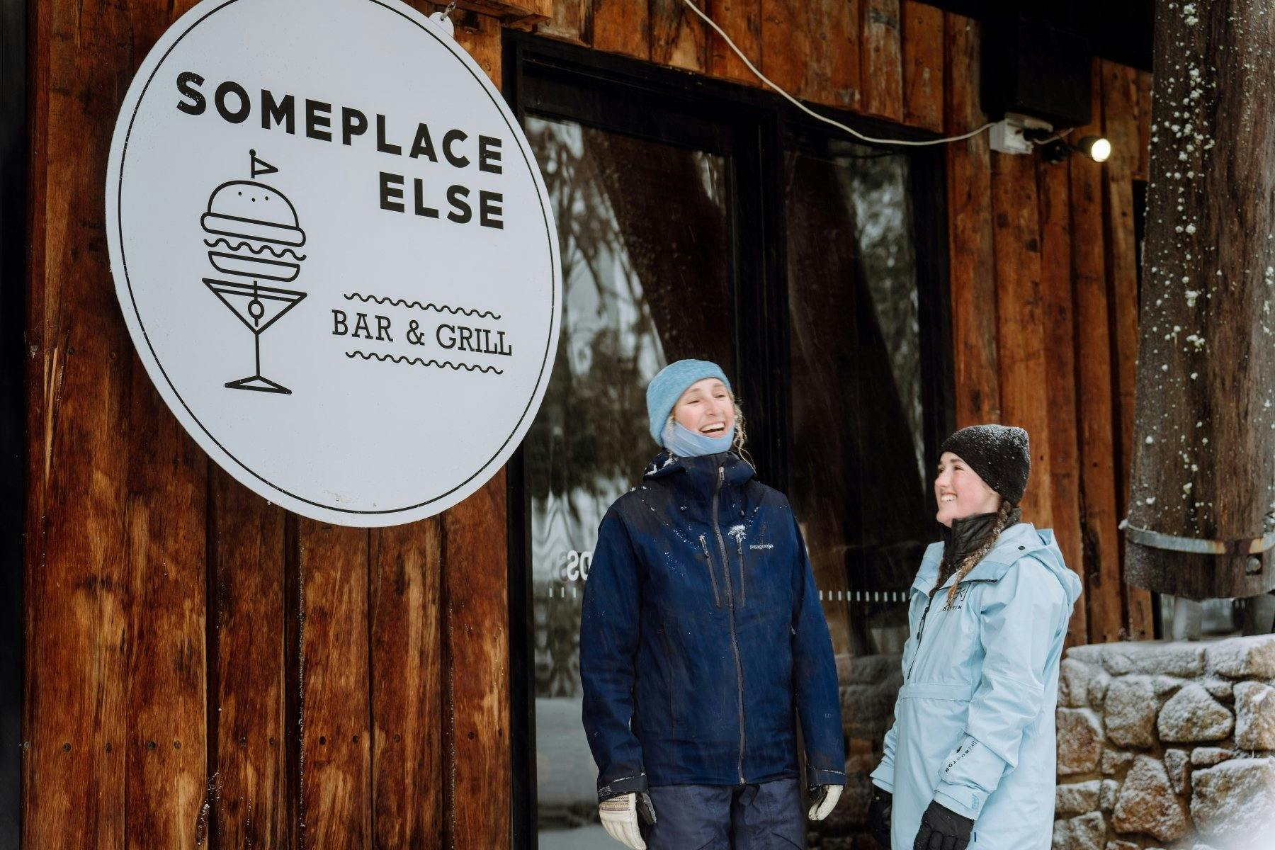two women smiling outside the main entrance of someplace else bar and grill