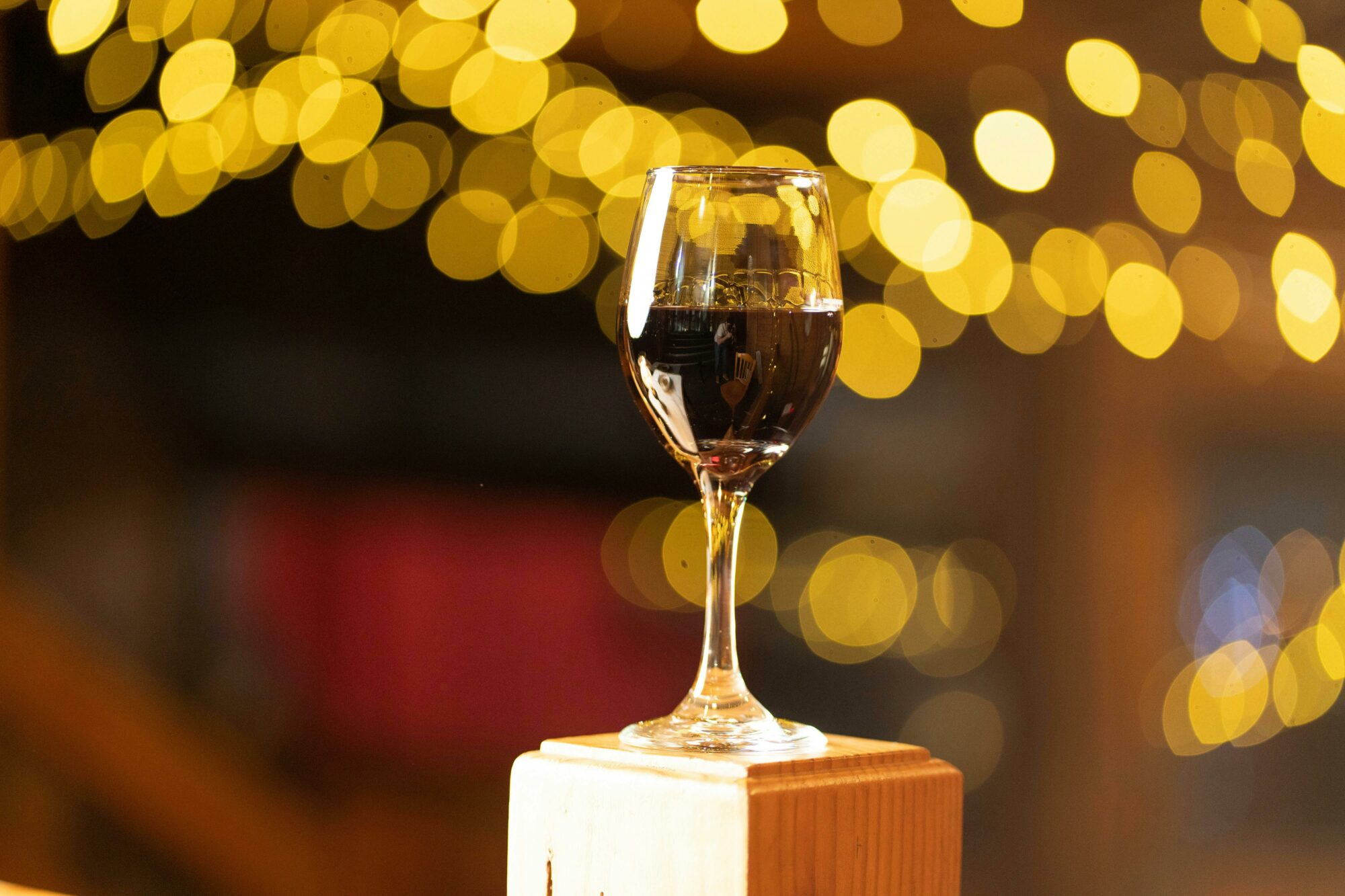 a glass of wine on a wooden block with fairy lights in the background