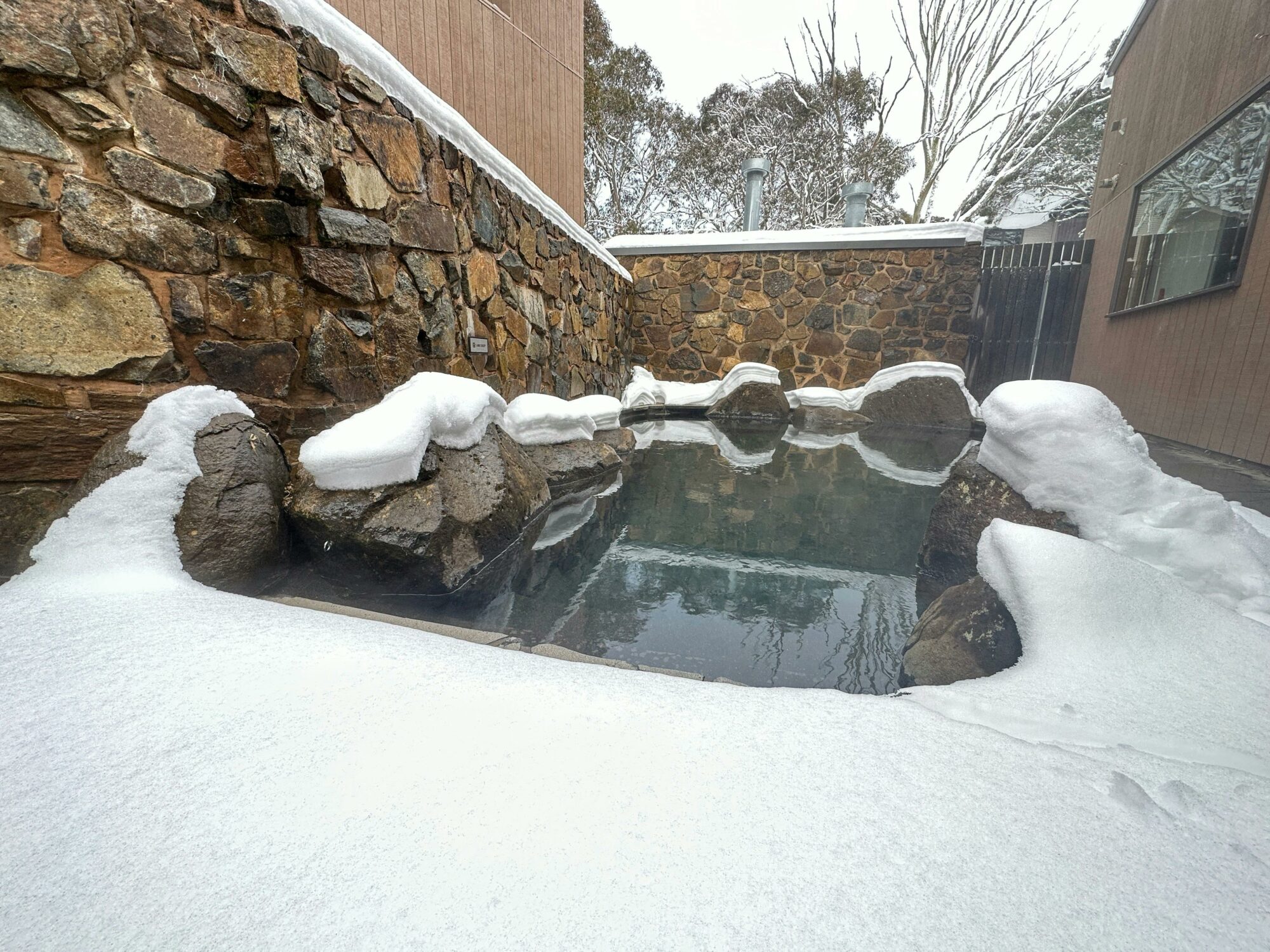 Onsen with snow around it and a stone wall