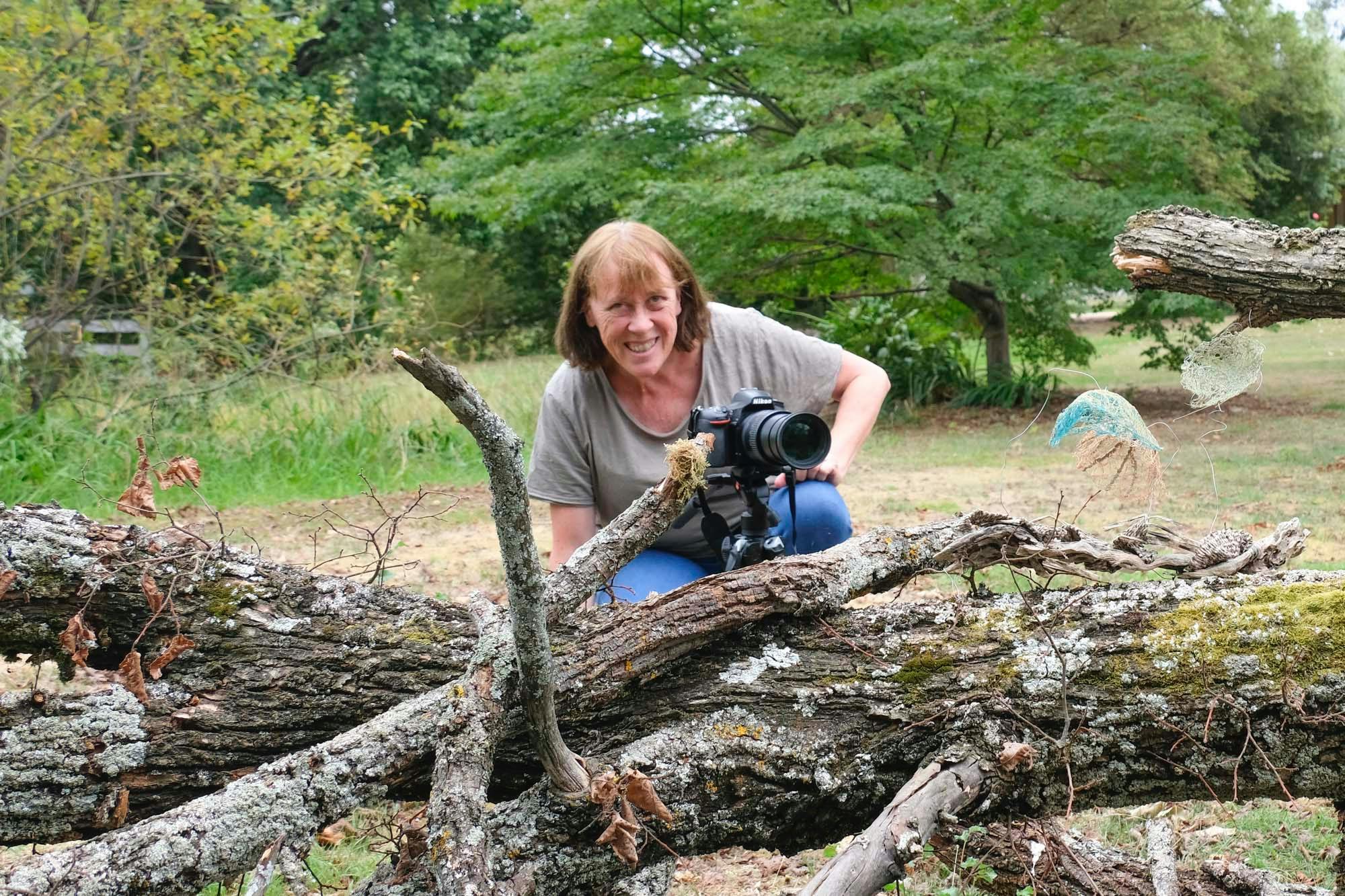 artist crouched by dead tree holding camera.