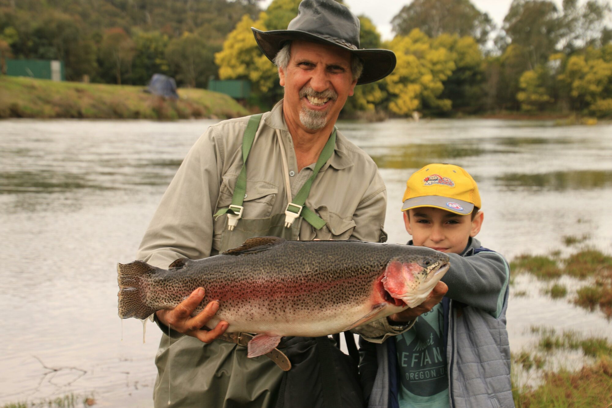 Rainbow trout held by a smiling man with a child next to him