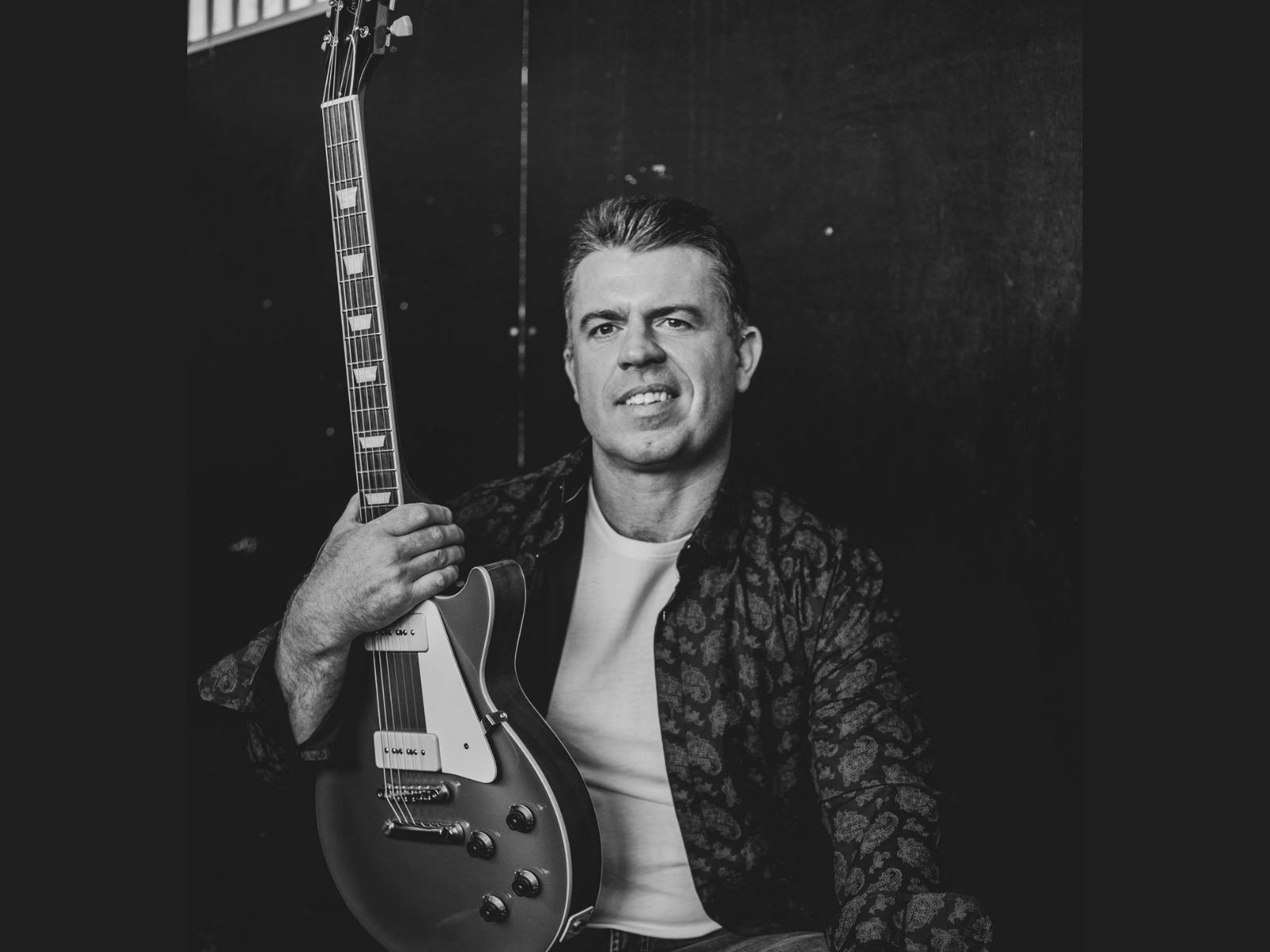Aaron Oldaker posing with an electric guitar.