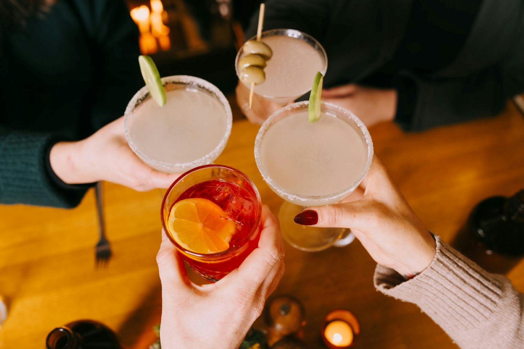 four cocktails being held up to cheers including margaritas with lime