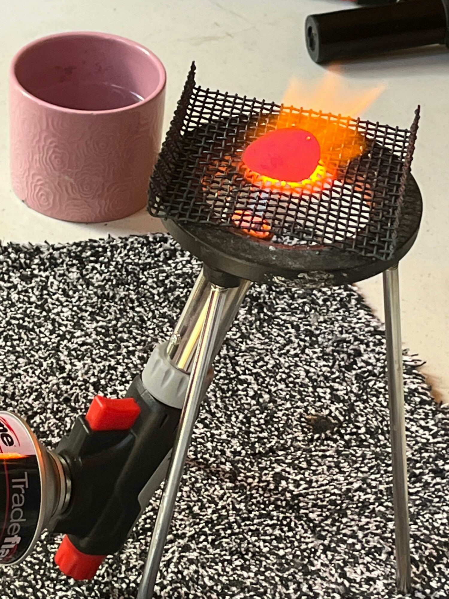A piece of copper is being heated until it glows bright red using a large blowtorch.