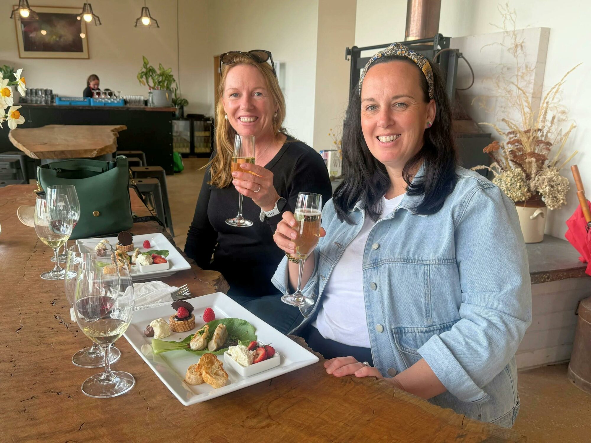 Two Women sitting next to each other with three dishes in front of them and three wine glasses
