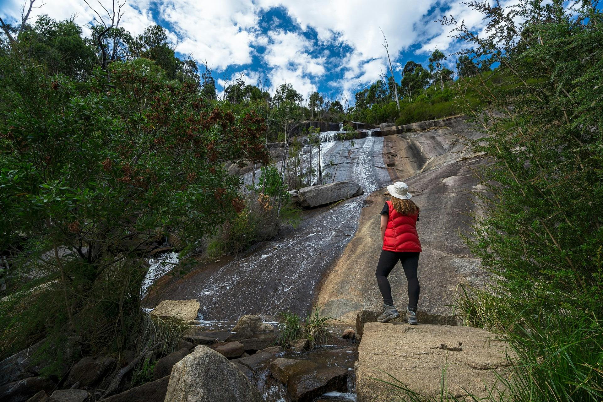 Person stading at the base of a waterfall surrounded by forest