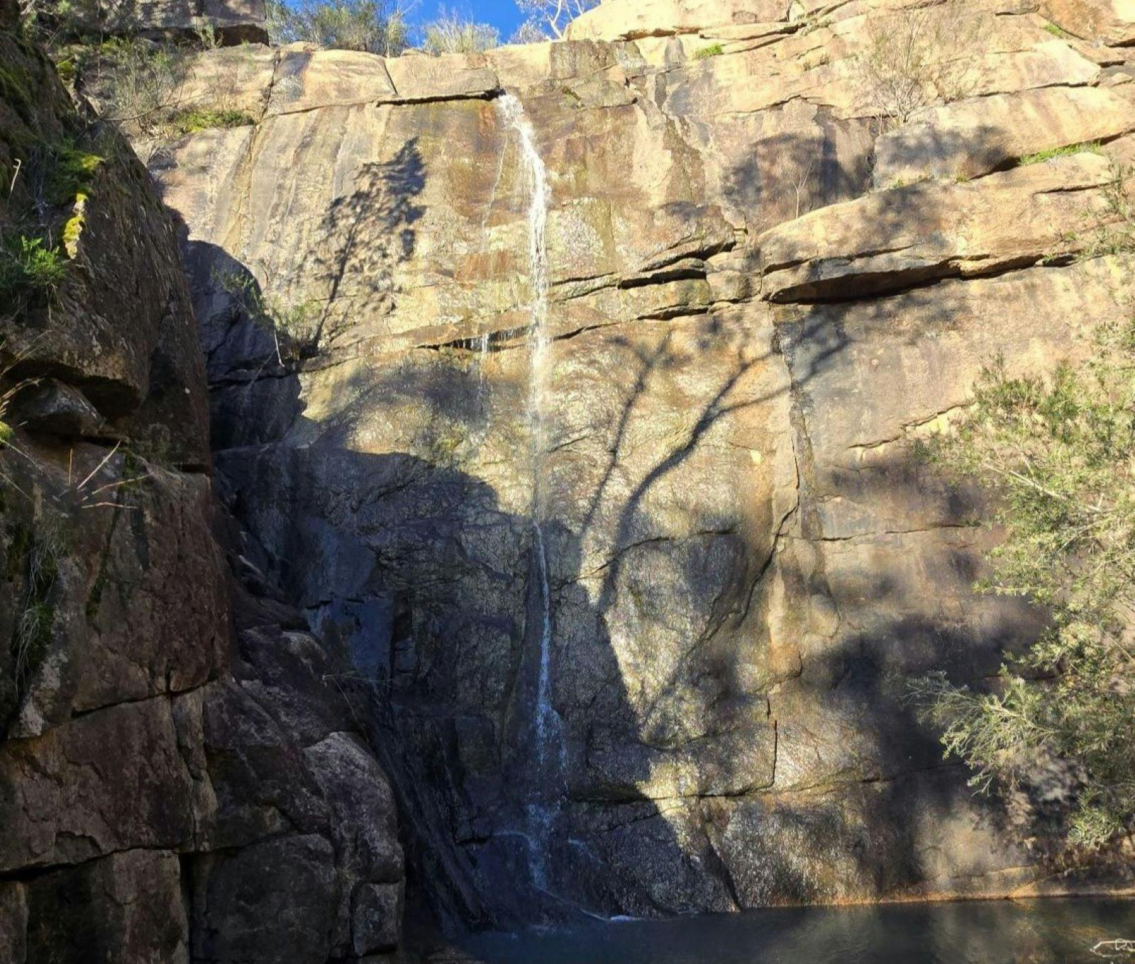 Rock face with small stream of water running vertically down it.