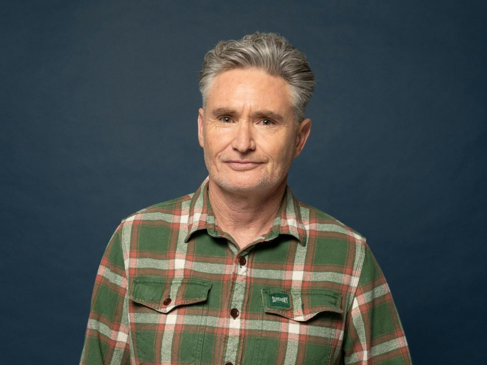 Comedian Dave Hughes standing in front of a dark background