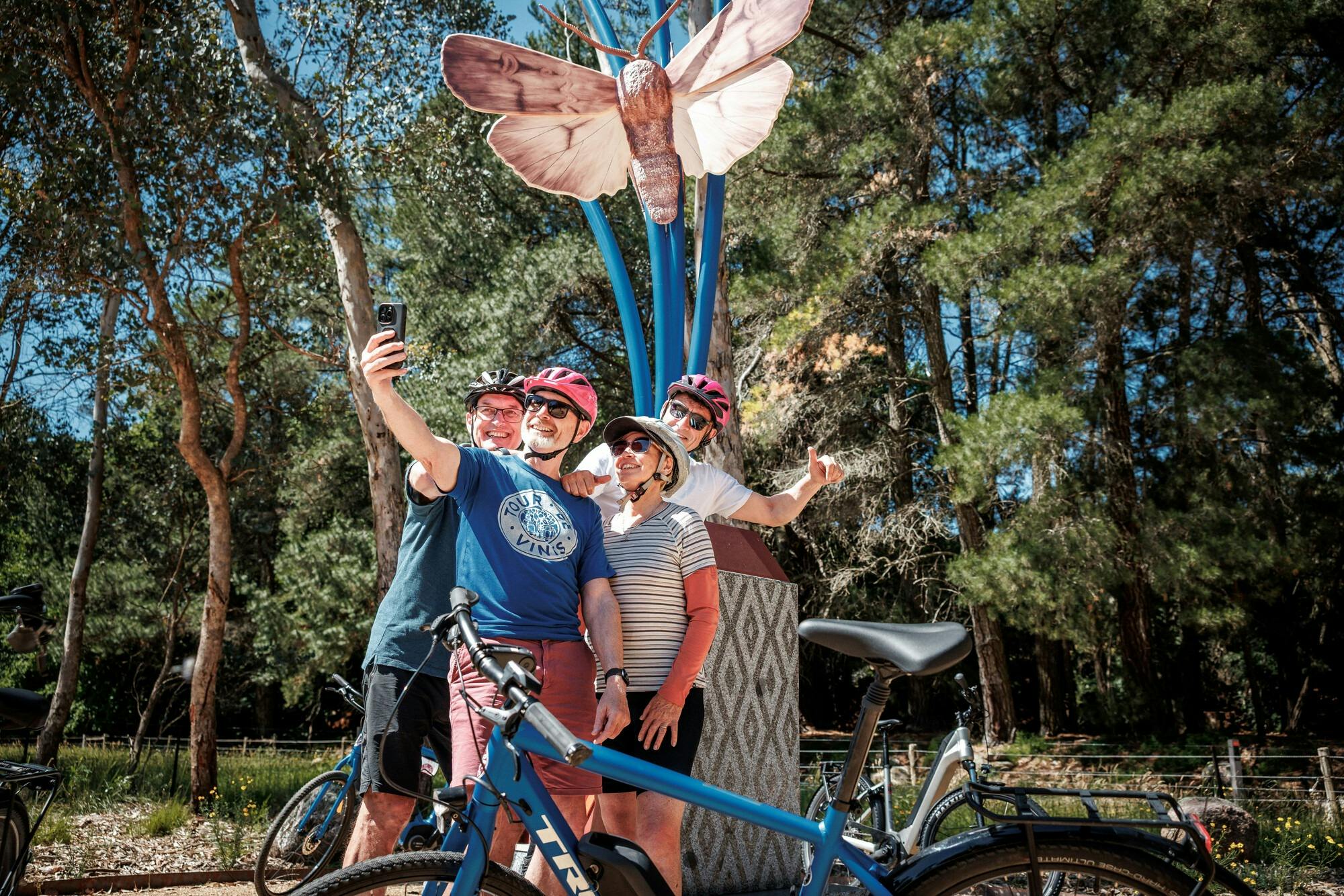 A group of cyclists taking a selfie infront of a sculpture of a Bogong Moth on a plinth