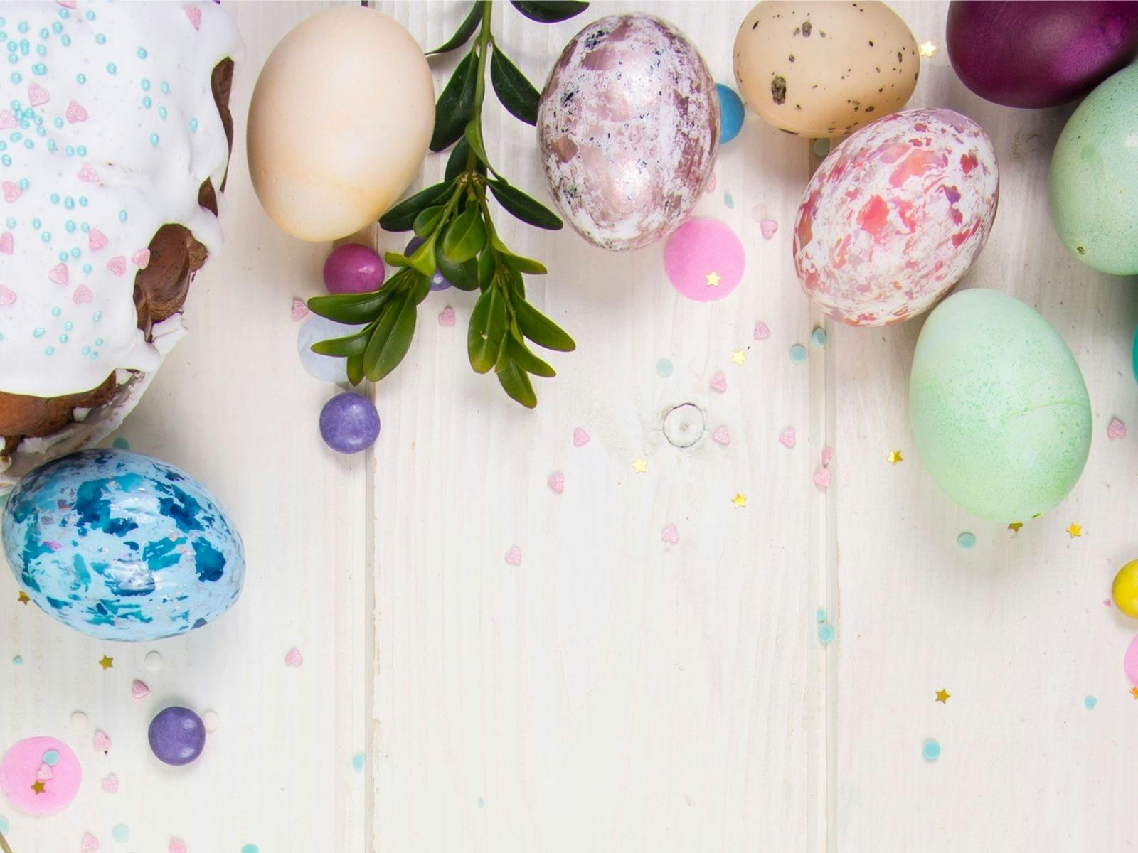 Iced cake, green sprig & decoupage eggs in blue, purple, green tones on a white wooden table