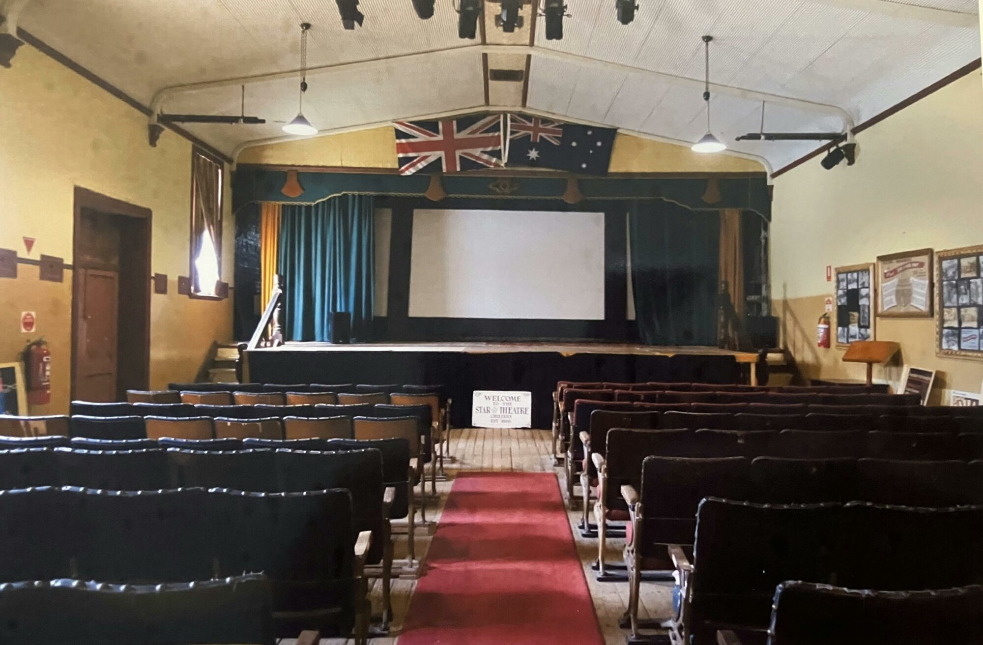 red carpet down aisle stage with film screen and blue curtains, British & Australian flags above