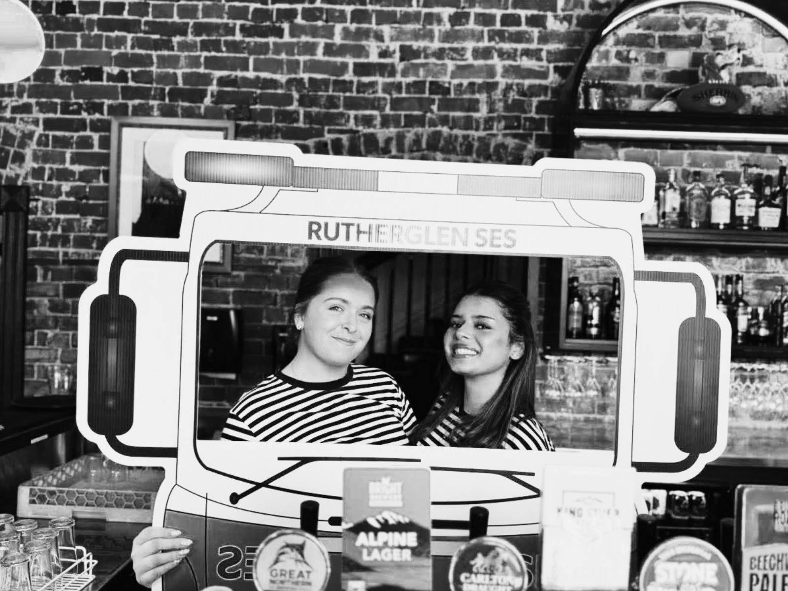 Two women dressed in Victoria Hotel uniform holding a Rutherglen SES cardboard cutout.