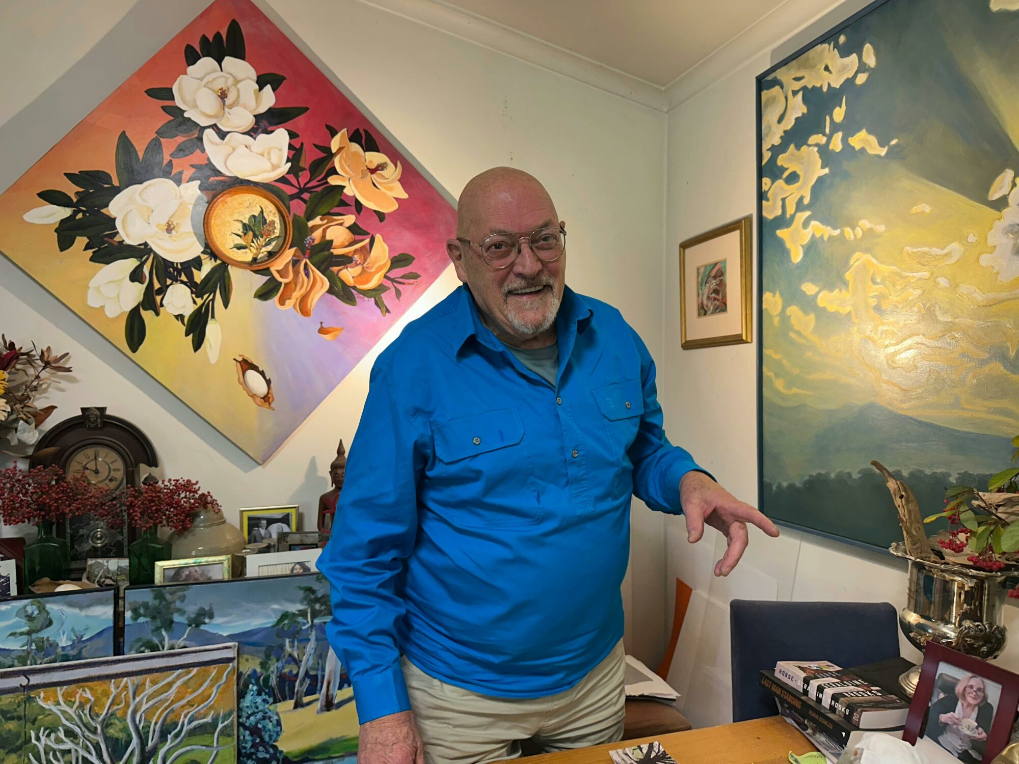 A man in a blue shirt posing in front of his artworks