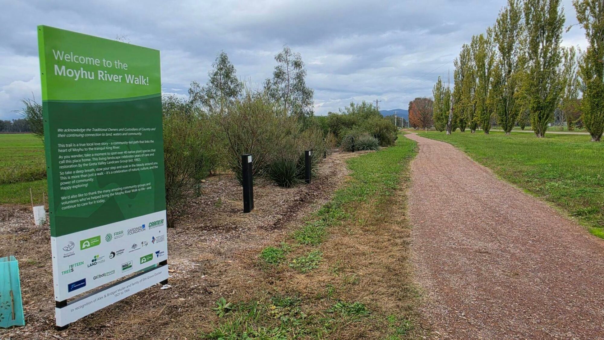 Large green sign saying 'Welcome to the Moyhu River Walk' next to a gravel path lined with grass