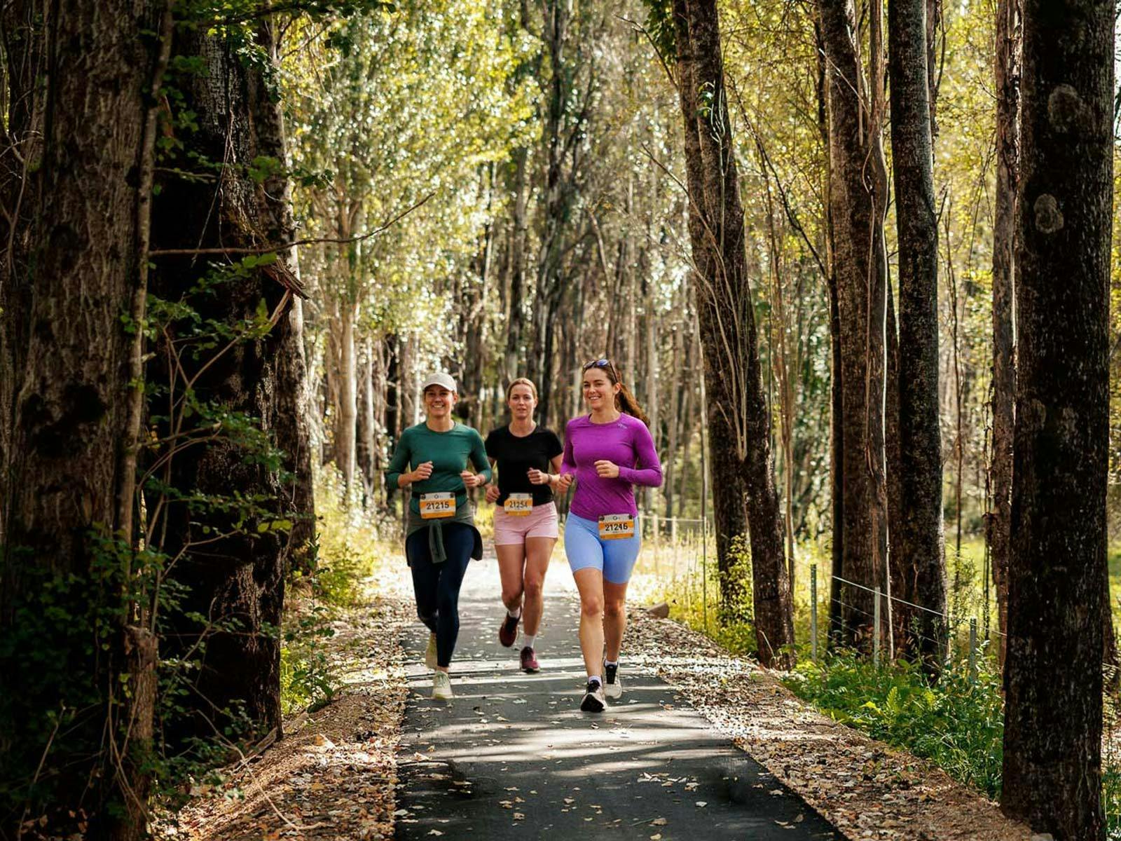 Three female runners on a trail through the trees