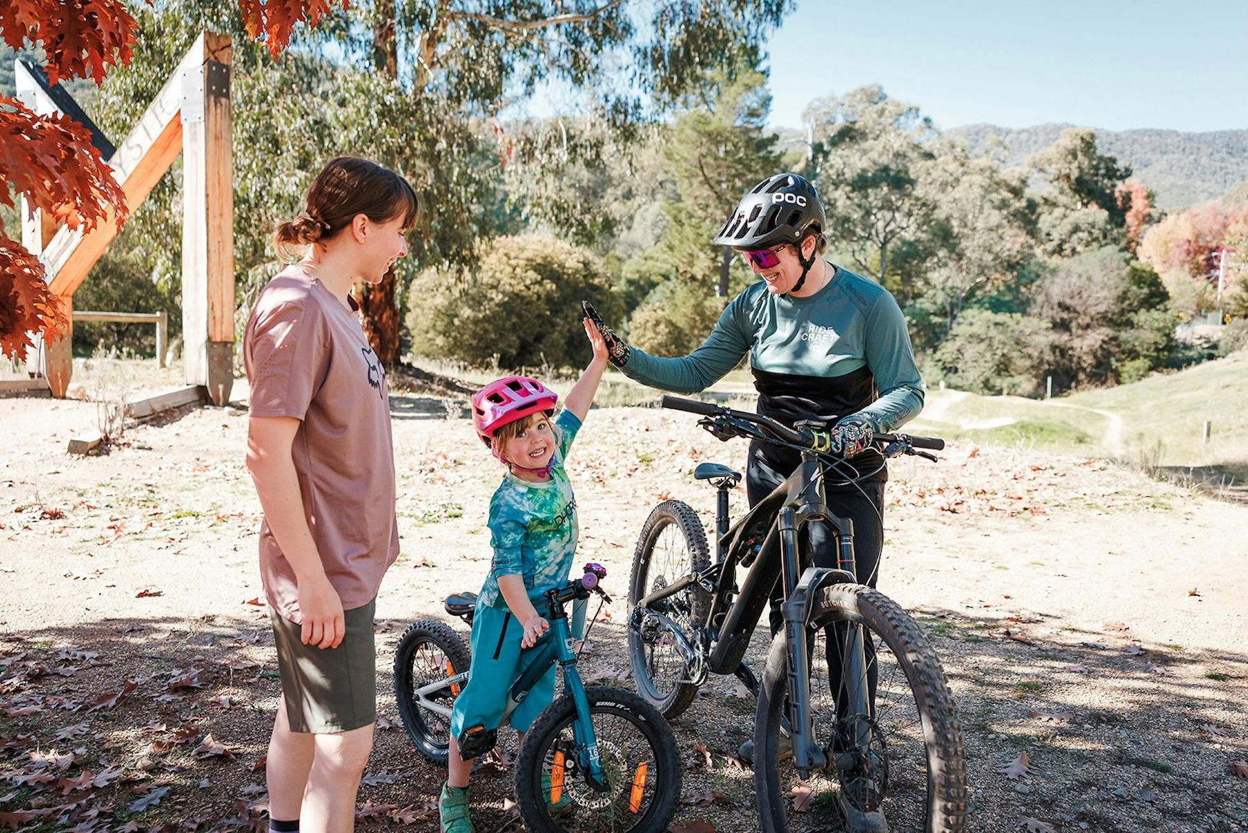 A young child with a bike high fives a coach with a bike while a woman looks on.
