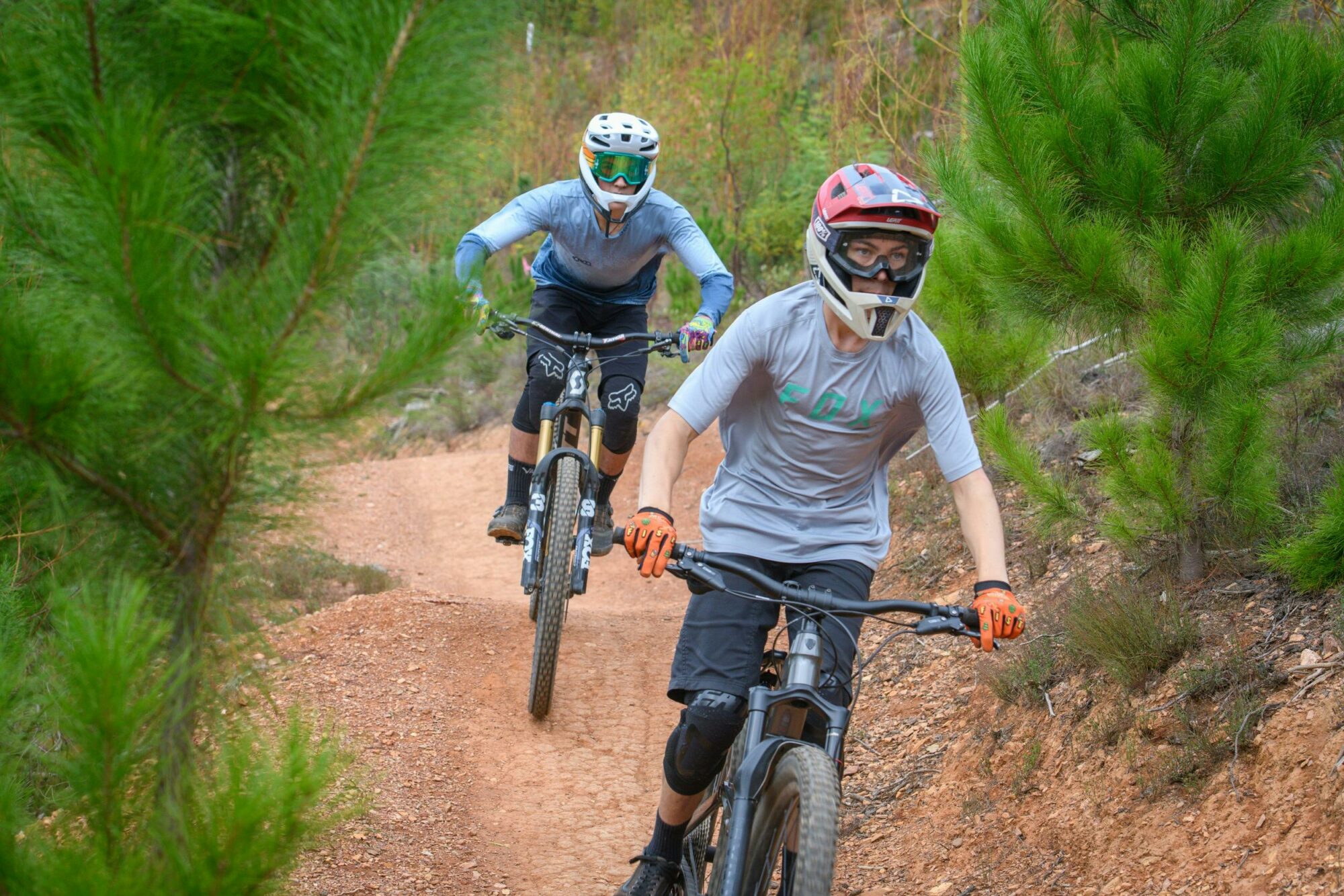 A group of mountain bike riders in full-face helmets descend a trail.