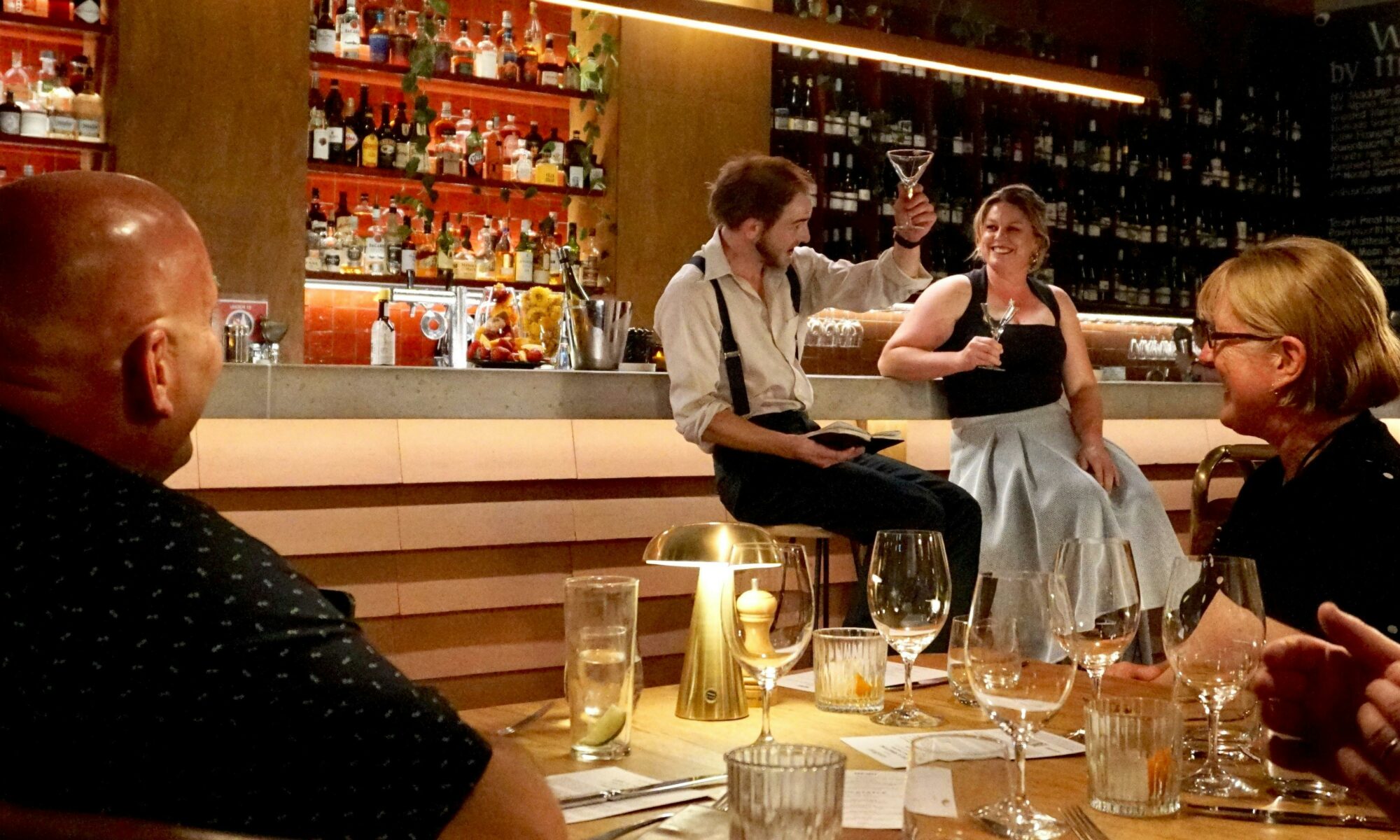 Performing Bartender raises a glass with audience participant at the bar