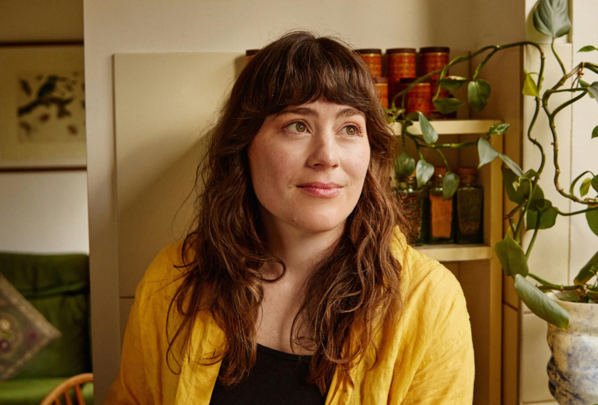 Lucy Wise looks towards window with trailing plant