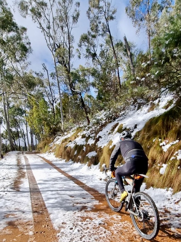 Gravel cyclist climbing with snow on the ground on a sunny day